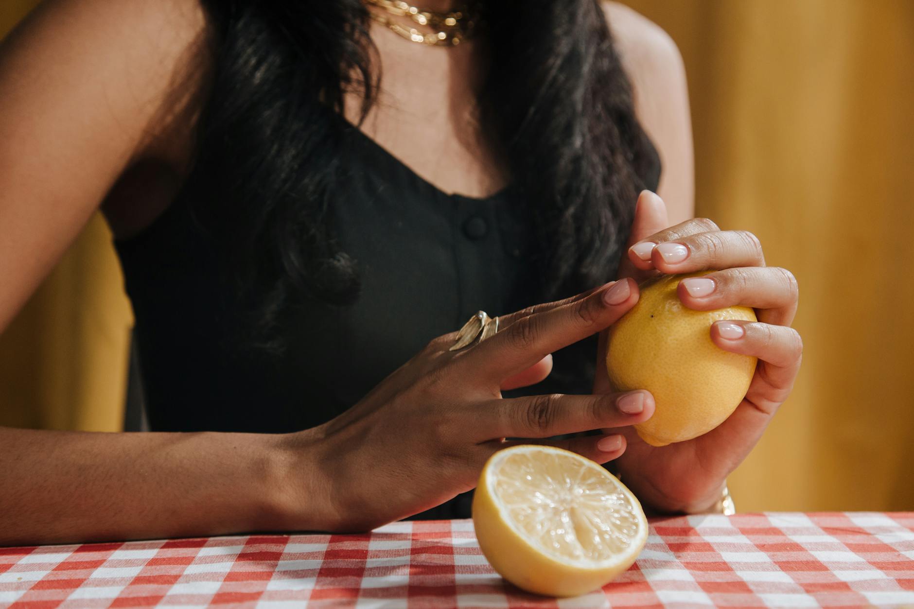 Close-up of a woman thoughtfully holding a fresh lemon at the table.