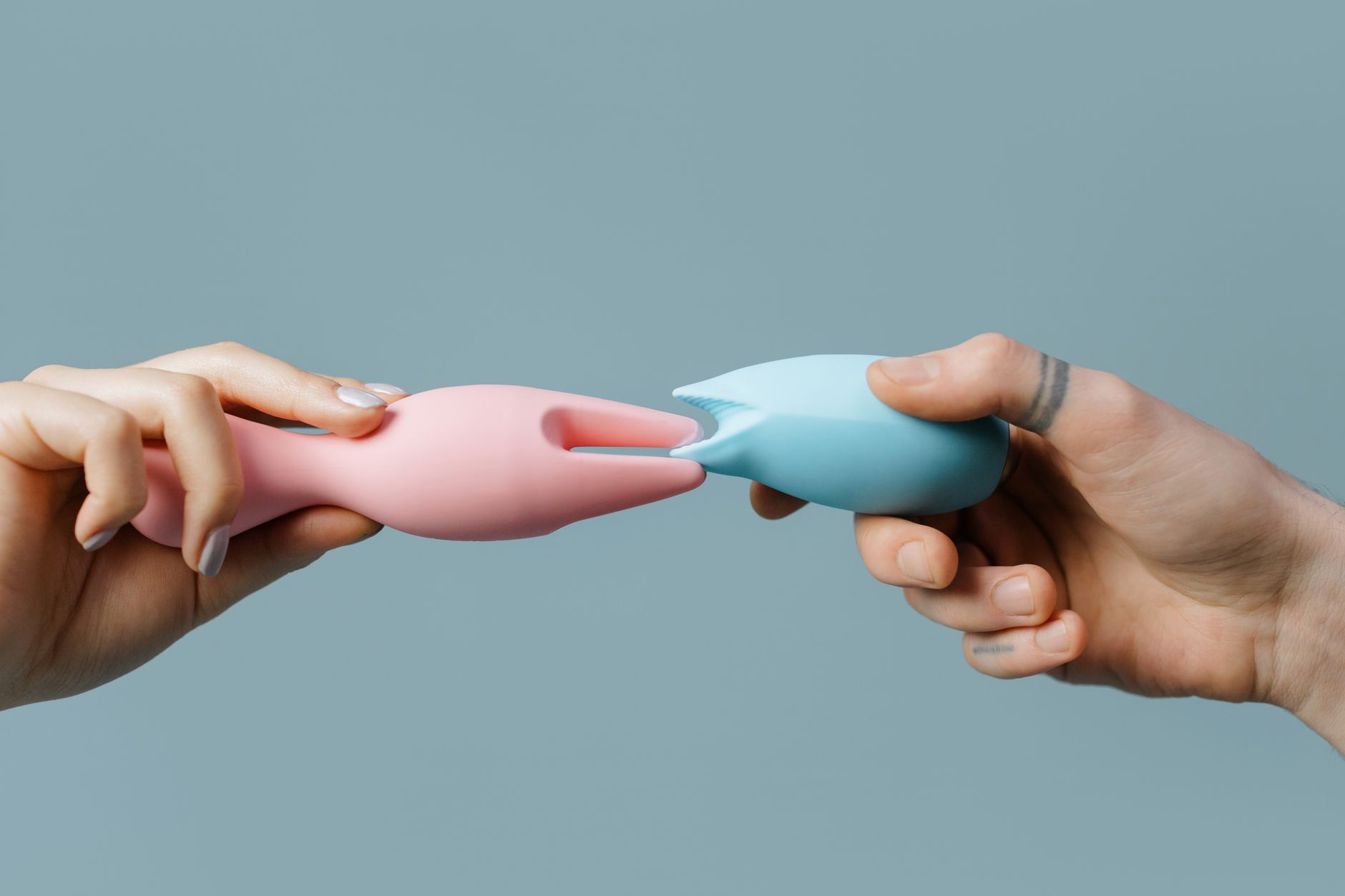Person holding two colorful vibrators against a purple background
