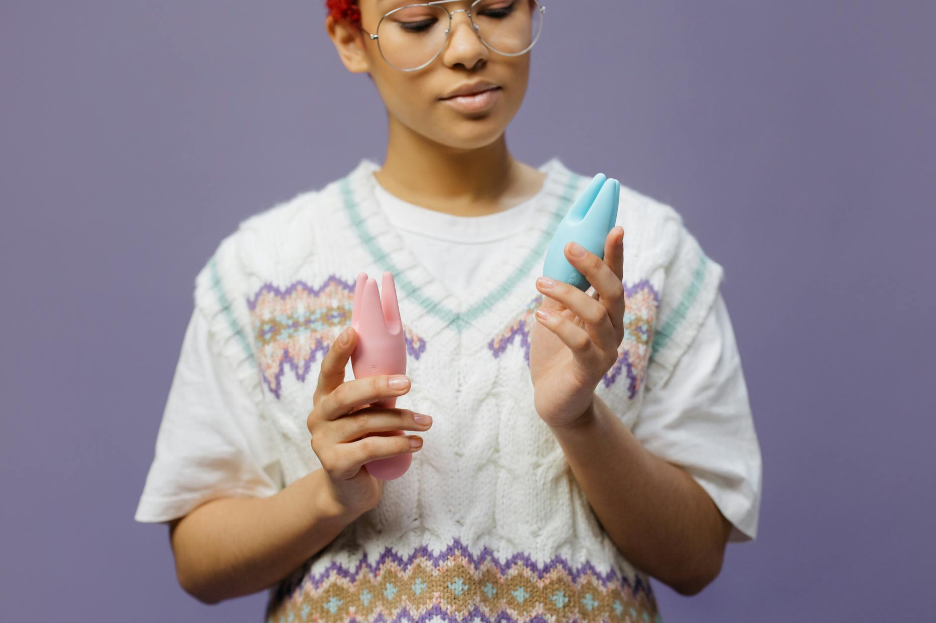 Woman holding blue and pink silicone vibrators in a contemplative gesture